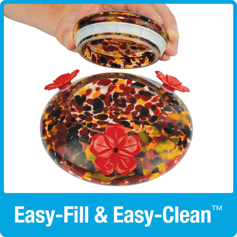 Load image into Gallery viewer, hand lifting the glass lid off of the base dish for easy fill and easy clean on the Nature&#39;s Way red, yellow and black speckled hand blown glass garden hummingbird feeder
