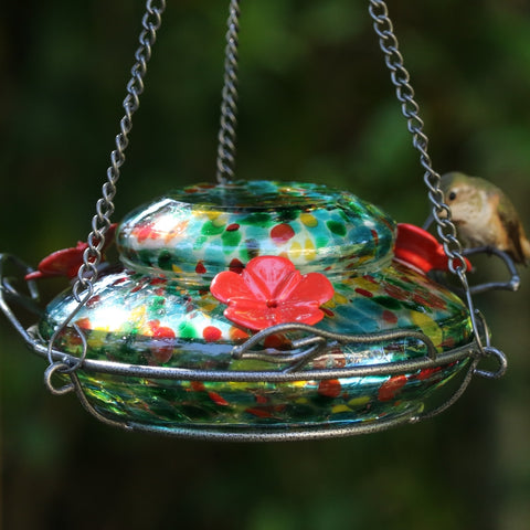 hummingbird feeding from Nature's Way hand blown glass garden hummingbird feeder in ocean sunset colors, red, yellow, green and red speckled hand blown glass